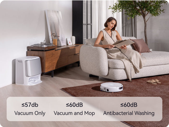Woman sitting on a couch reading a book with Narwal Flow robot vacuum cleaner in the foreground, showing different noise level labels.