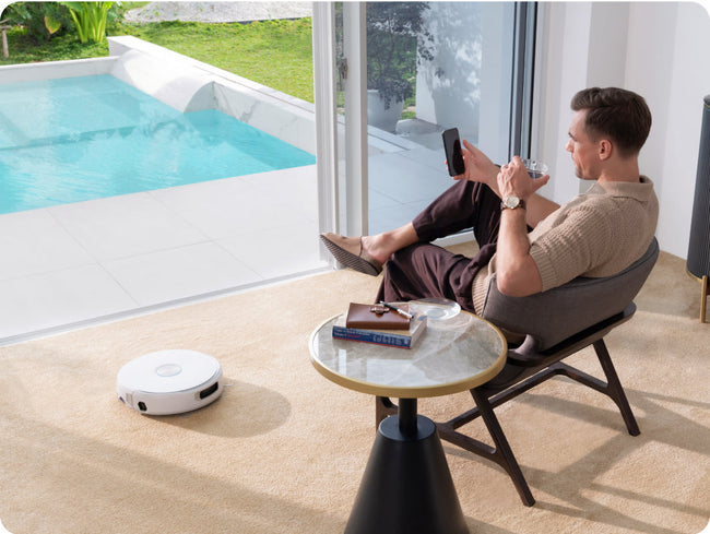 Man sitting by a pool with Narwal Flow robot vacuum cleaner on the floor.