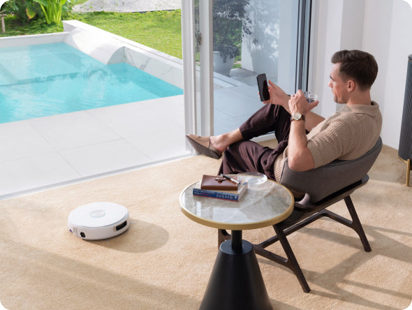 Man sitting by a pool with Narwal Flow robot vacuum cleaner on the floor.